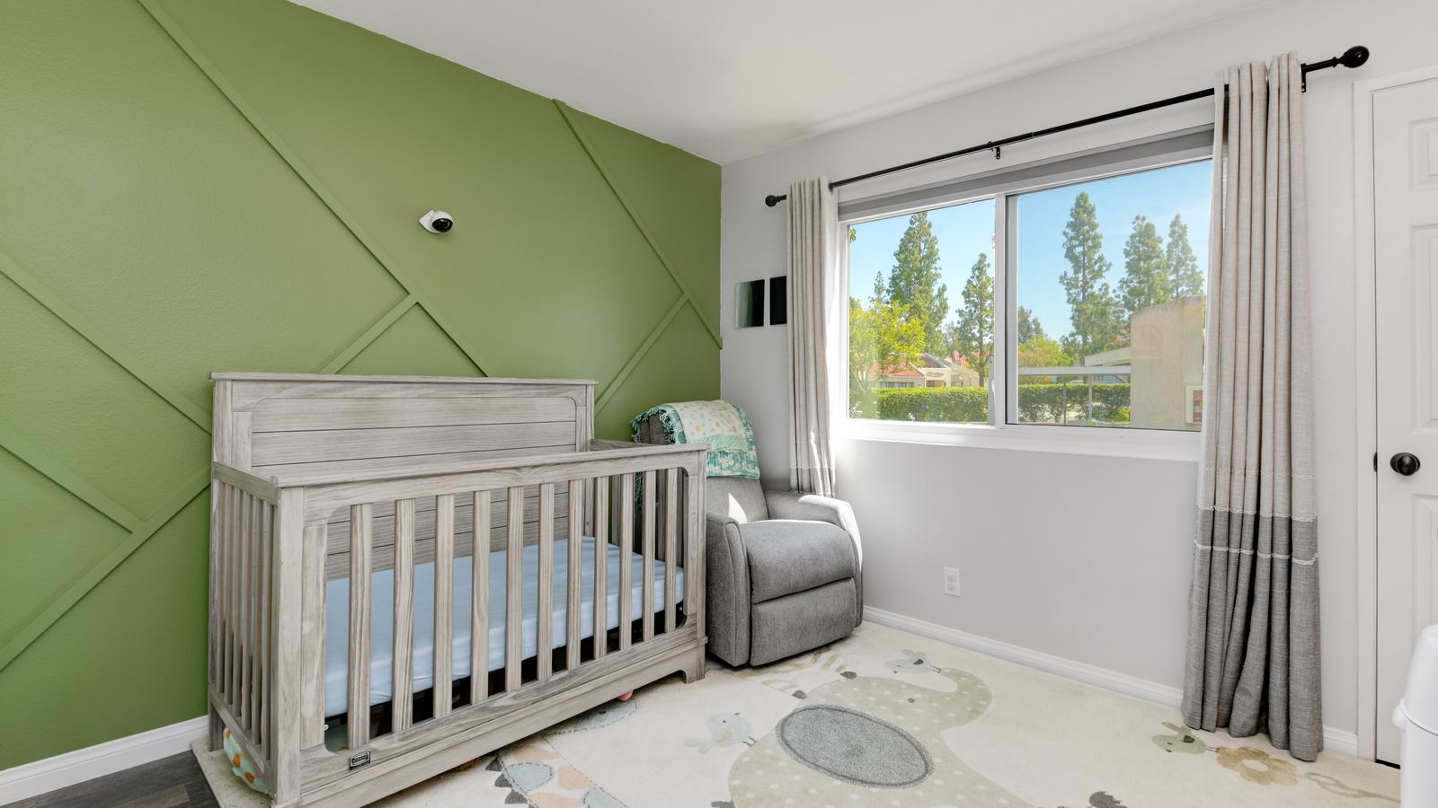 Nursery with a green accent wall and a crib